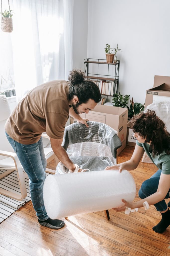A couple packing furniture with bubble wrap in an apartment, preparing for relocation.