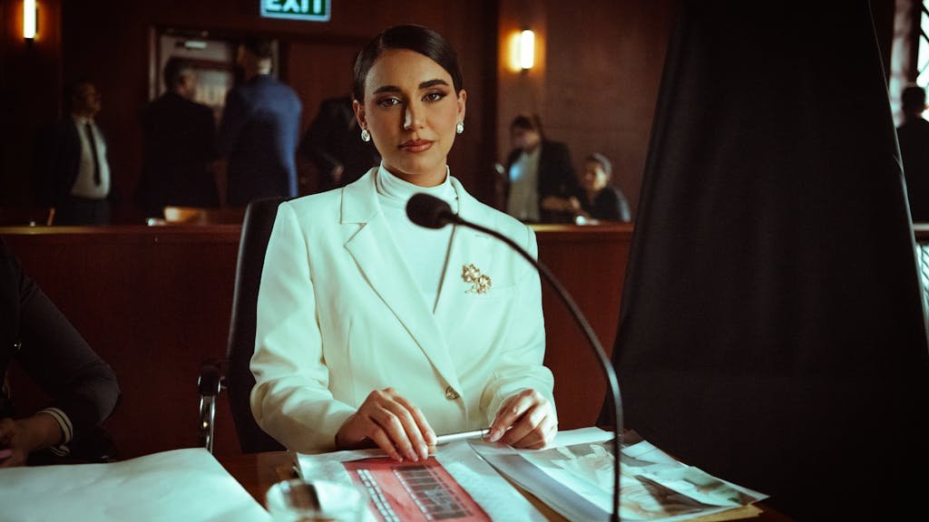 A poised woman in a white suit sits confidently in a courtroom setting, Baghdad.