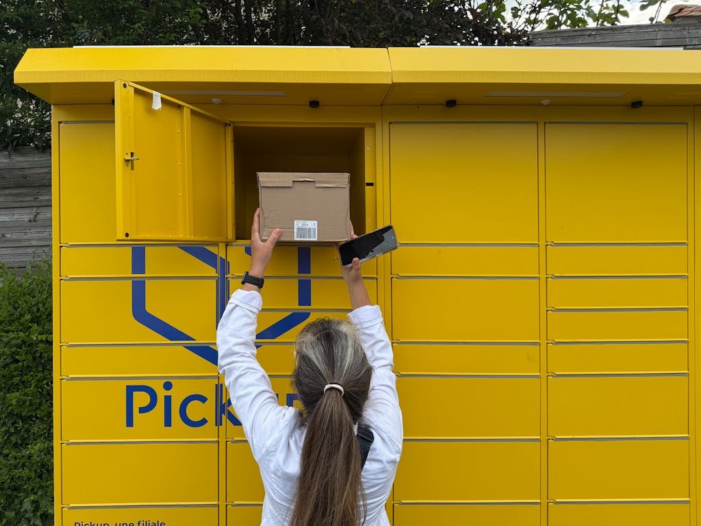 A woman using a yellow parcel locker to pick up a package in Périgueux, France.