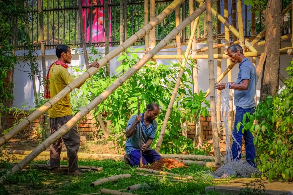 Three men collaborate to build a large bamboo structure in an outdoor setting.