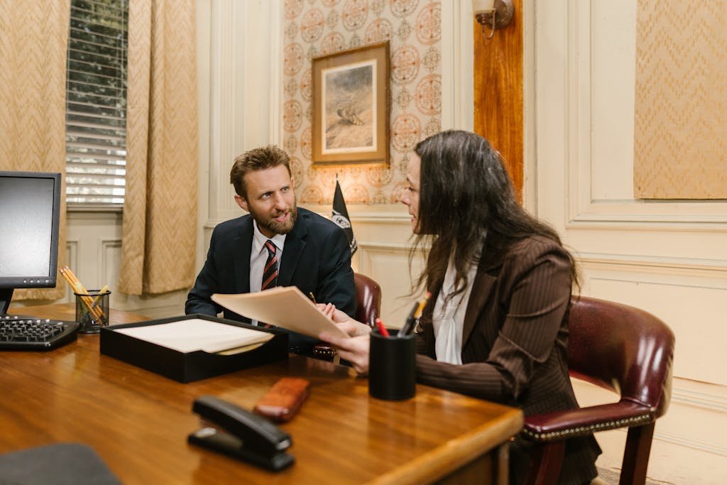Two professionals engaged in a business discussion in an office setting, reviewing legal documents.